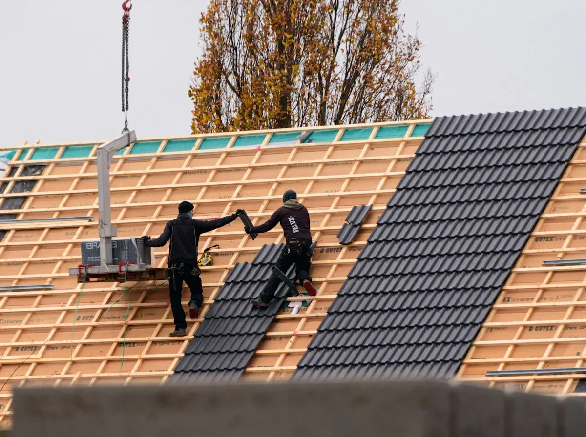 Roof Replacement in El Monte — two roofers laying dark roof tiles on new battens beside a hoist
